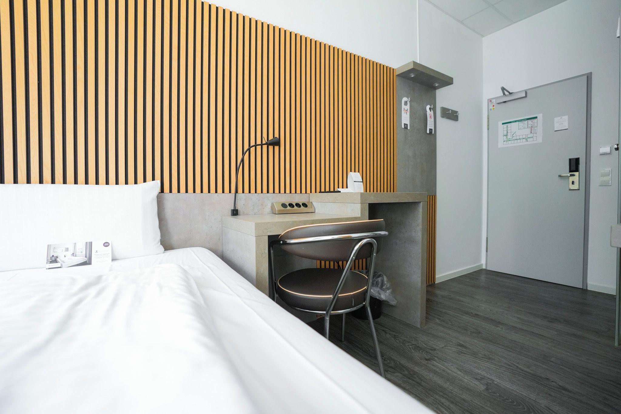 A hotel room with a bed, a desk, a chair, and a wardrobe.