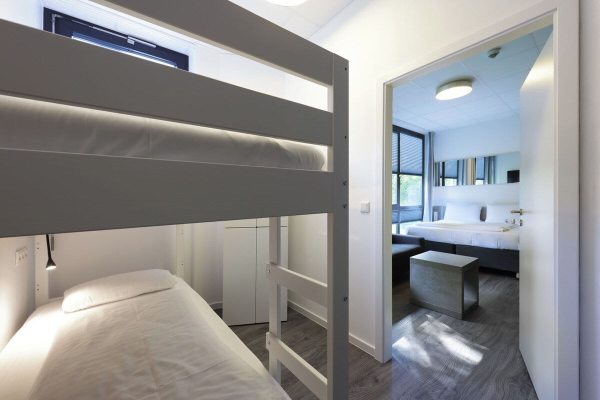 A bunk bed room with a view of a bathroom and a desk.