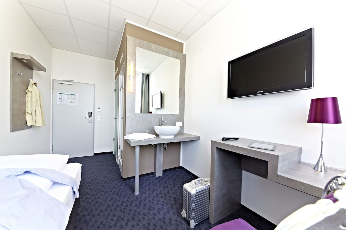 Una habitación de hotel con cama, baño con lavabo y espejo, televisor y maleta.