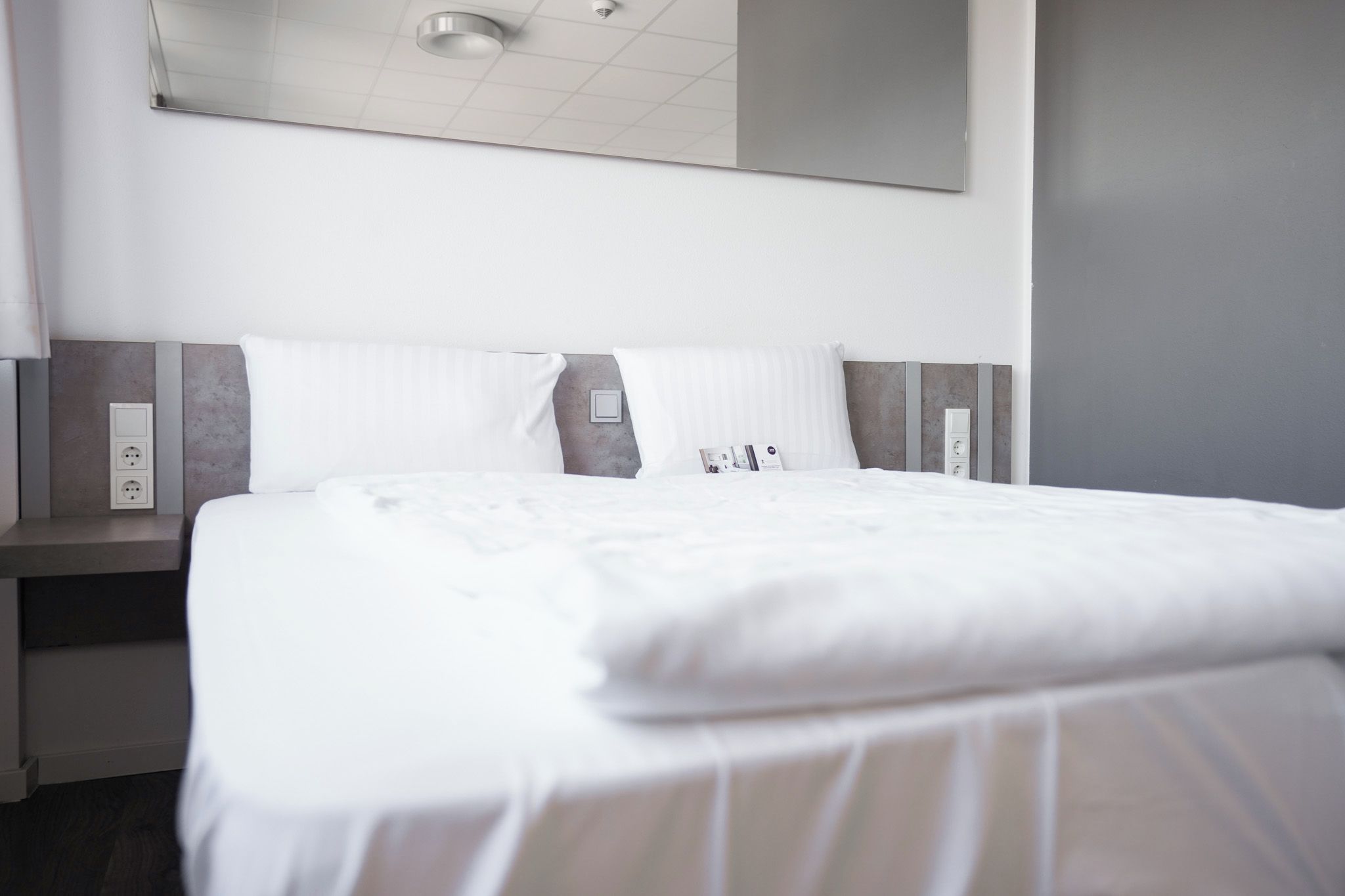 Une chambre d’hôtel avec un lit bien fait, une table de chevet avec une lampe et un panneau de commande fixé au mur.