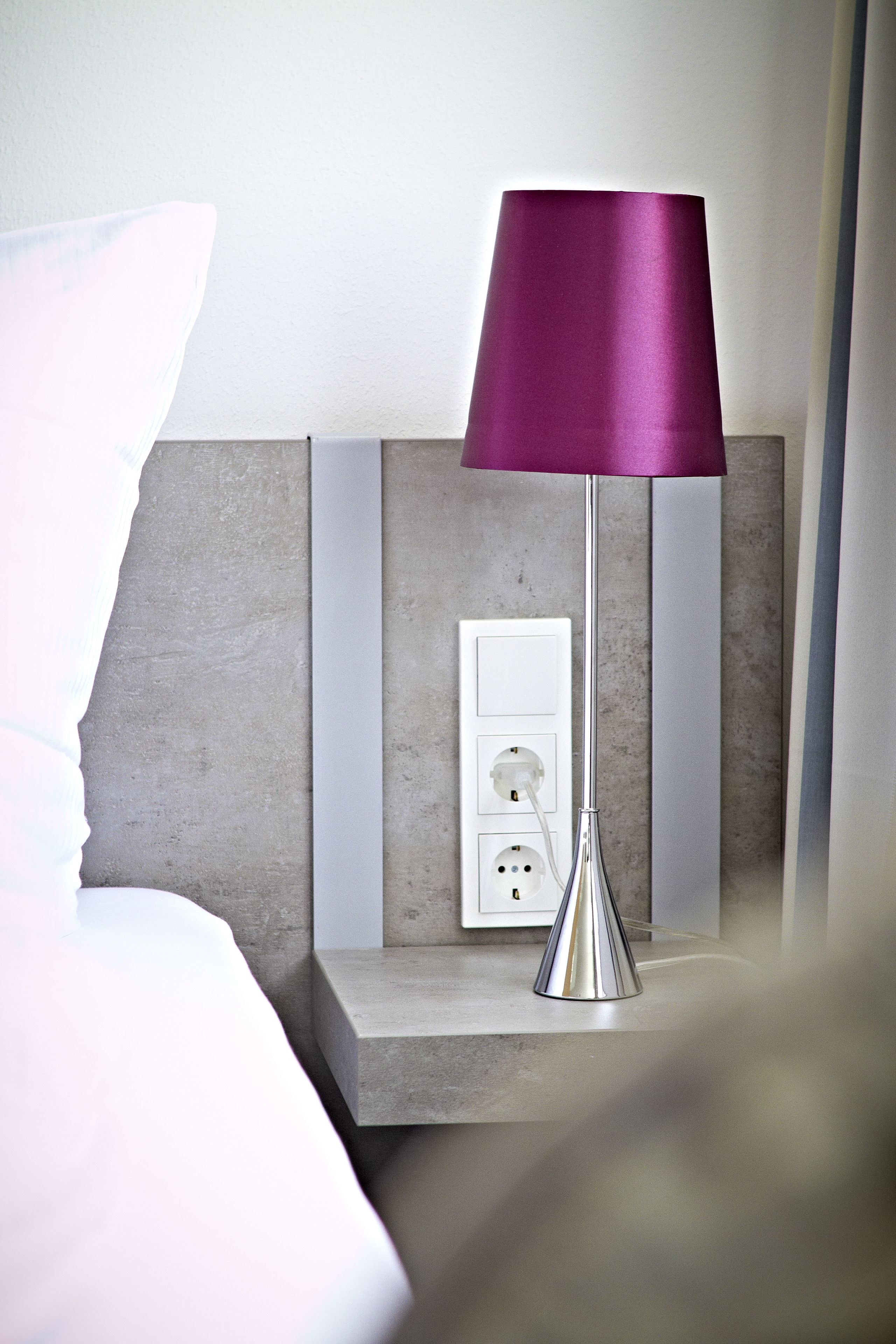 Une chambre d’hôtel moderne équipée d’une table de chevet, d’une lampe et d’une prise électrique.