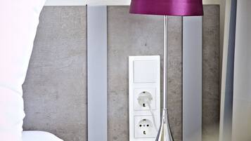 Une chambre d’hôtel moderne équipée d’une table de chevet, d’une lampe et d’une prise électrique.