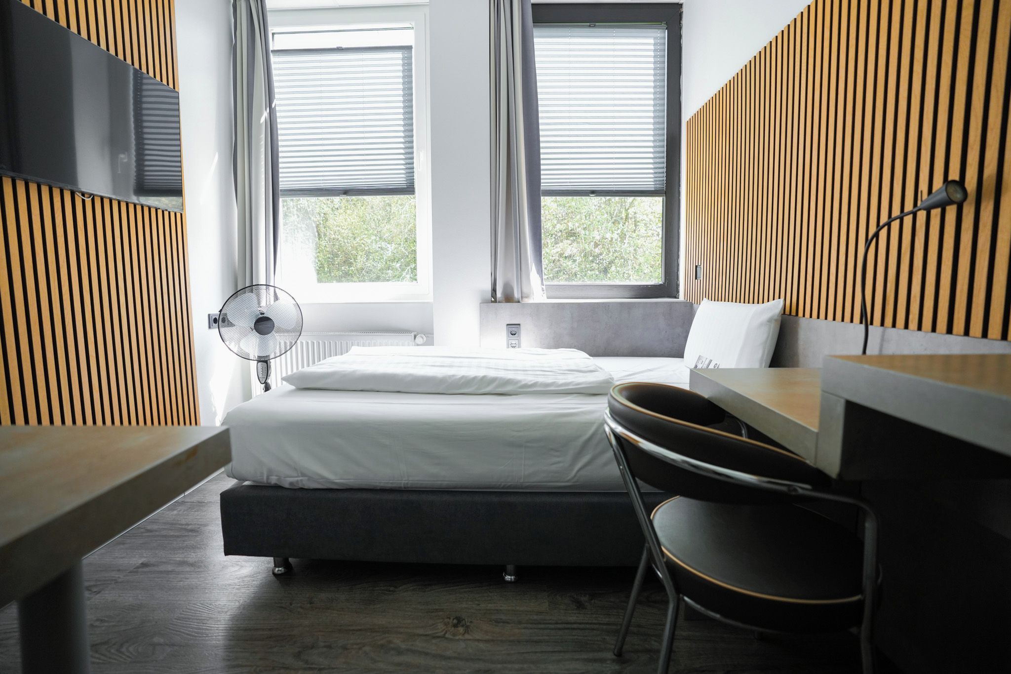 Een moderne slaapkamer met een bed, nachtkastje, stoel en een ventilator.