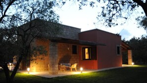 Ein modernes Haus mit Steinaußenwand und roter Fassade, ausgestattet mit einer Terrasse, Gartenmöbeln und Beleuchtung.