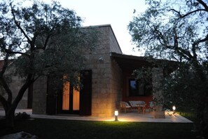 Un bâtiment moderne doté d’une façade en pierre, d’un patio couvert avec des sièges et d’une entrée bien éclairée.
