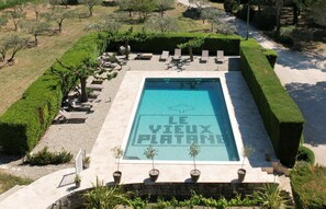 A rectangular swimming pool with a clear blue water surface, surrounded by a stone deck and a low stone wall. - Le Vieux Platane (Cairanne)