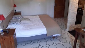 A bedroom with a bed, a nightstand, a red lamp, a water bottle, and a wooden dresser. - Le Vieux Platane (Cairanne)