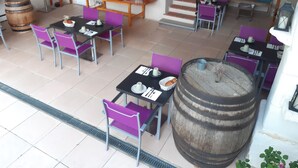 A spacious dining area with multiple tables and chairs, a central bar area with stools, and a staircase leading to an upper level. - Le Vieux Platane (Cairanne)