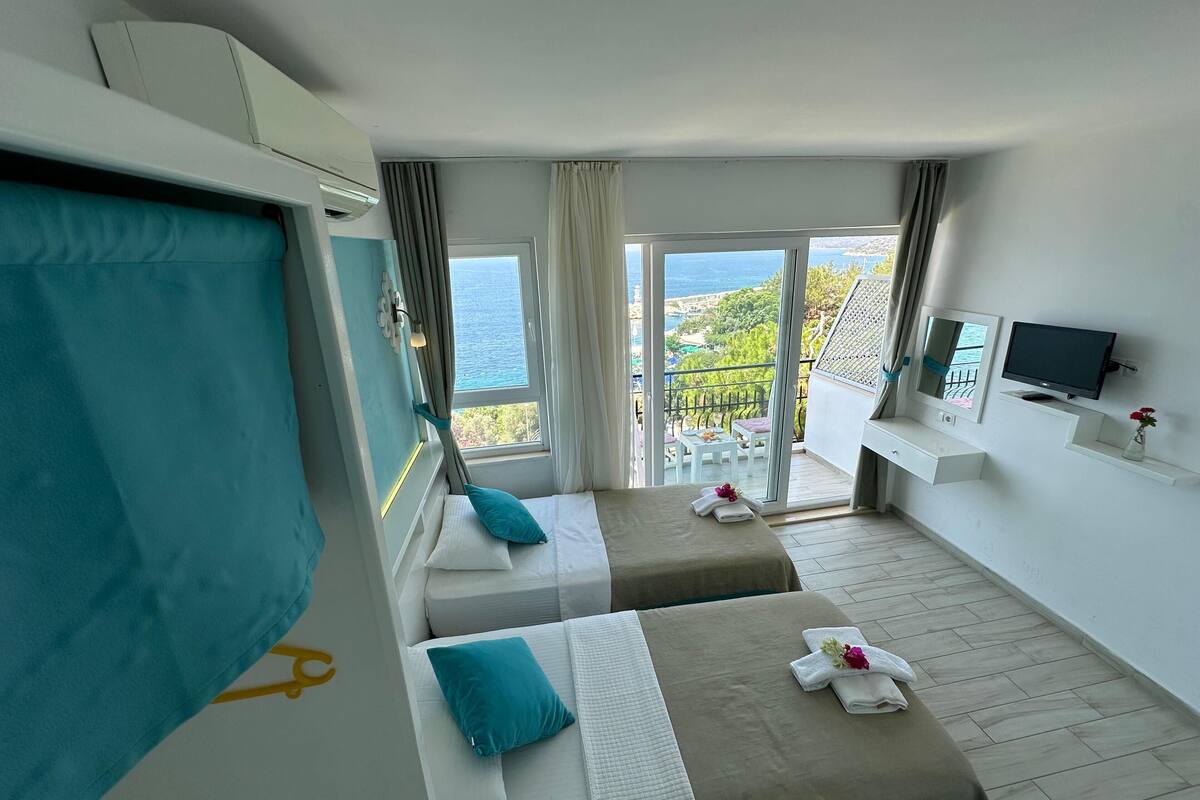 Une chambre d’hôtel avec deux lits, une télévision et un balcon donnant sur la mer.