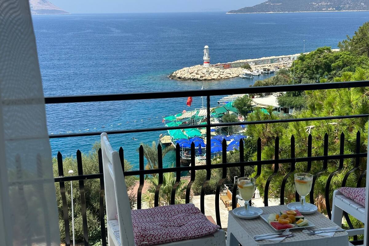 Un balcon avec une table dressée pour le dîner, donnant sur une zone côtière avec un phare et des bateaux.