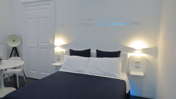 Une chambre d’hôtel comprenant un lit, deux lampes de chevet, un bureau avec une chaise et une lampe fixée au mur.