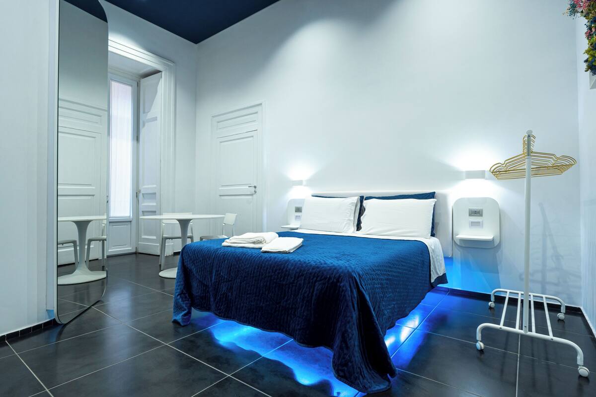 Moderni hotellihuone, jossa on suuri sänky, yöpöydät ja oleskelualue tuoleineen.