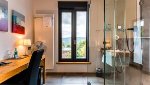 Habitación de hotel con escritorio, silla y un ventanal que ofrece vistas al exterior.