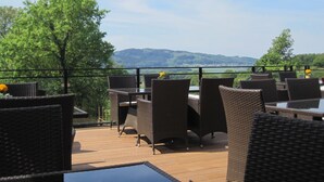 Un patio al aire libre con mobiliario de mimbre y vista a un lago y colinas.