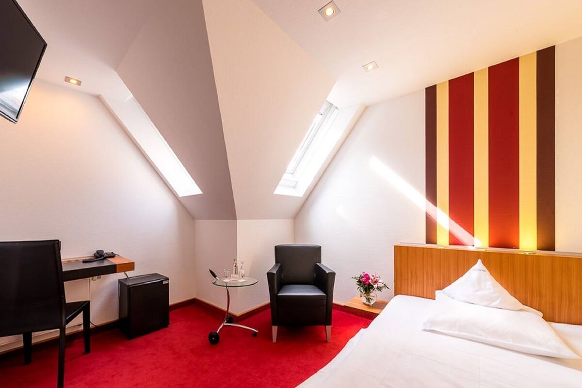 A hotel room with a bed, a desk, a chair, a small table, and a TV.