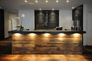 A hotel reception desk with a wooden design, a sign above it, and a vase with flowers on the left. - Hotel Antoniushuette (Balve)