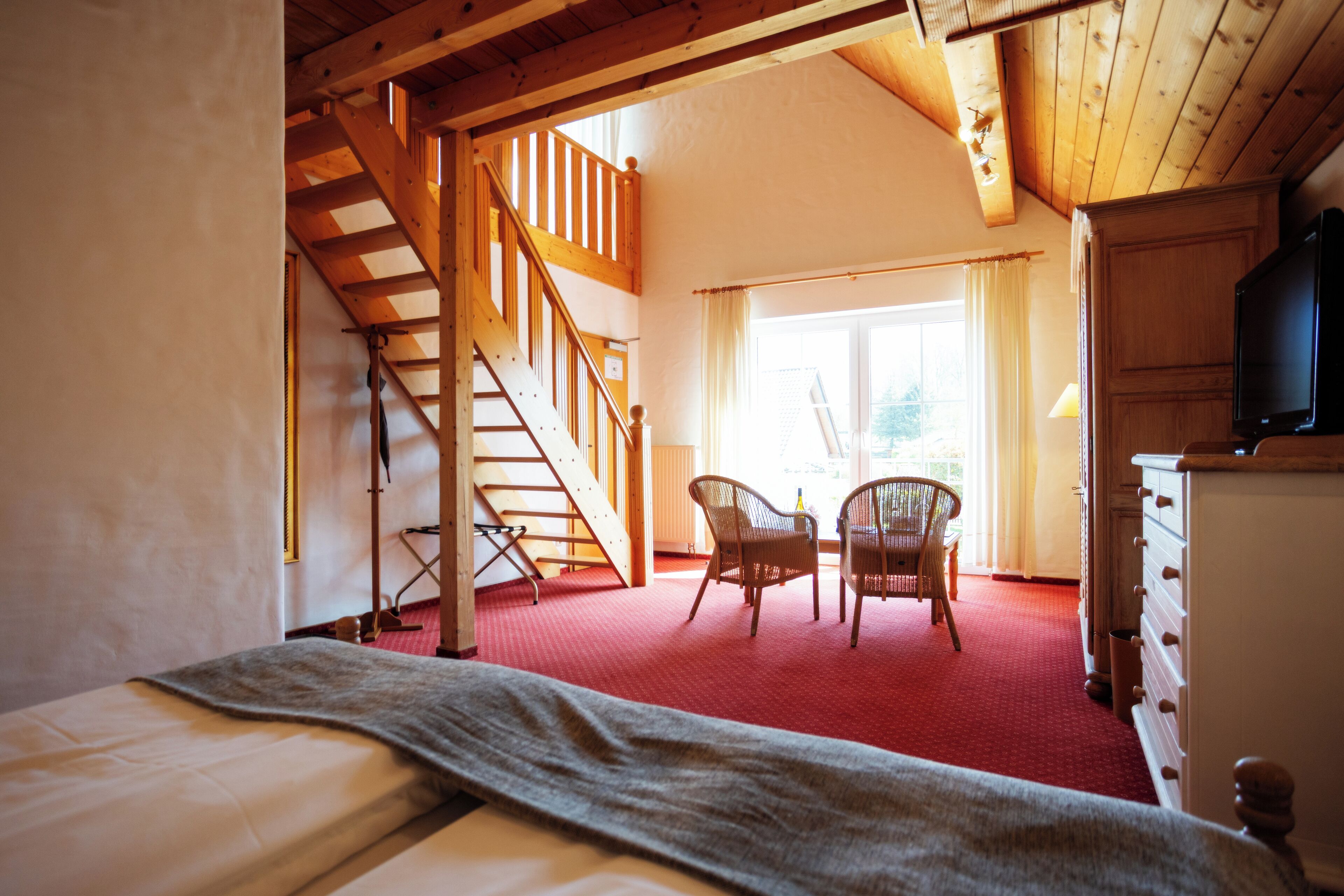 A room with a bed, a staircase, a dining area with chairs, and a television.