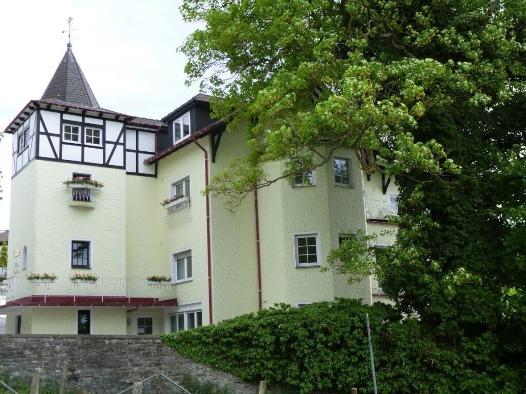 Ein mehrstöckiges Gebäude mit einem markanten Turm, Balkonen und einer Steintreppe, die zum Eingang führt.