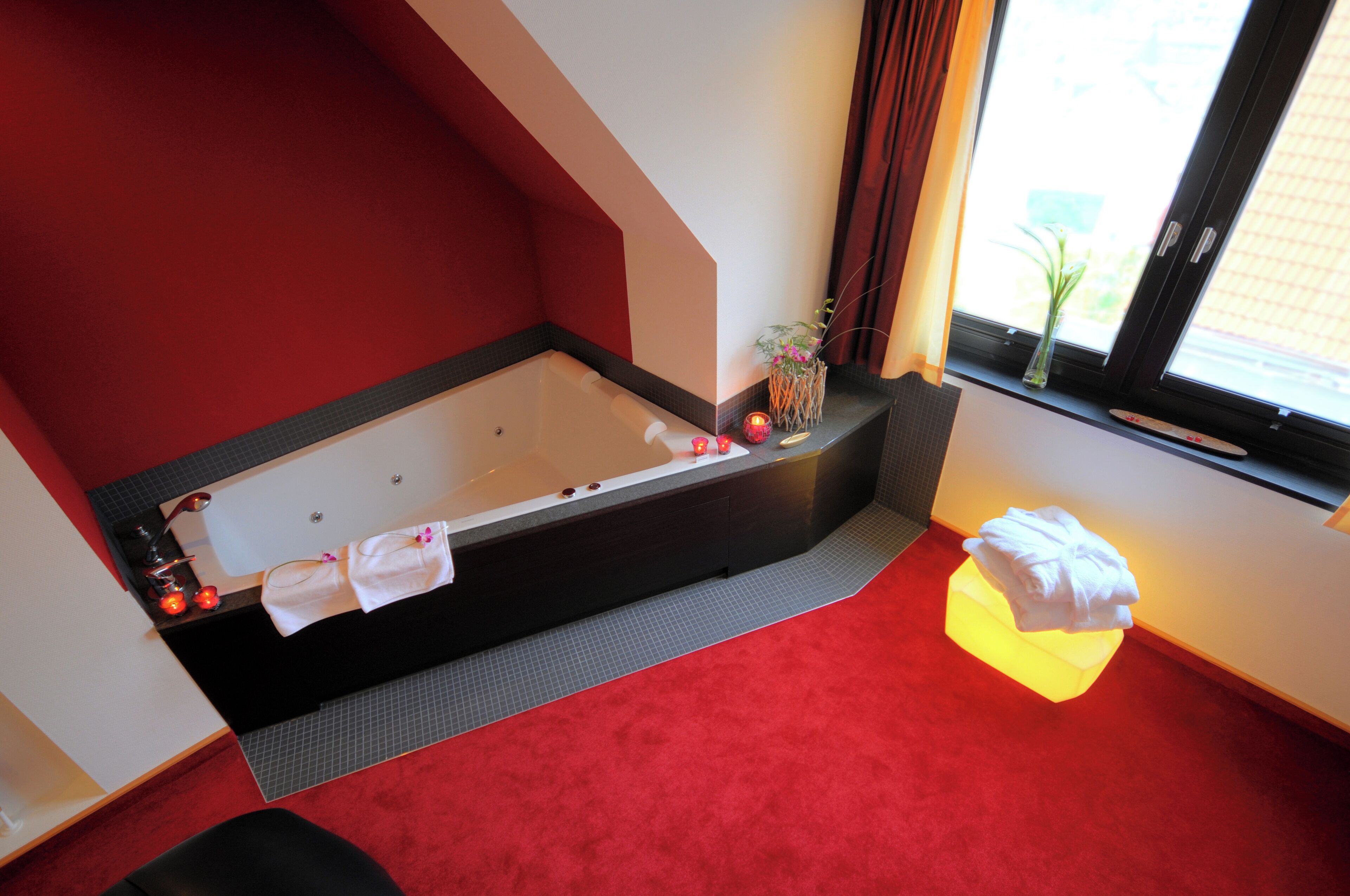 A modern bathroom with a large bathtub, a small table with a vase, and a red carpet.