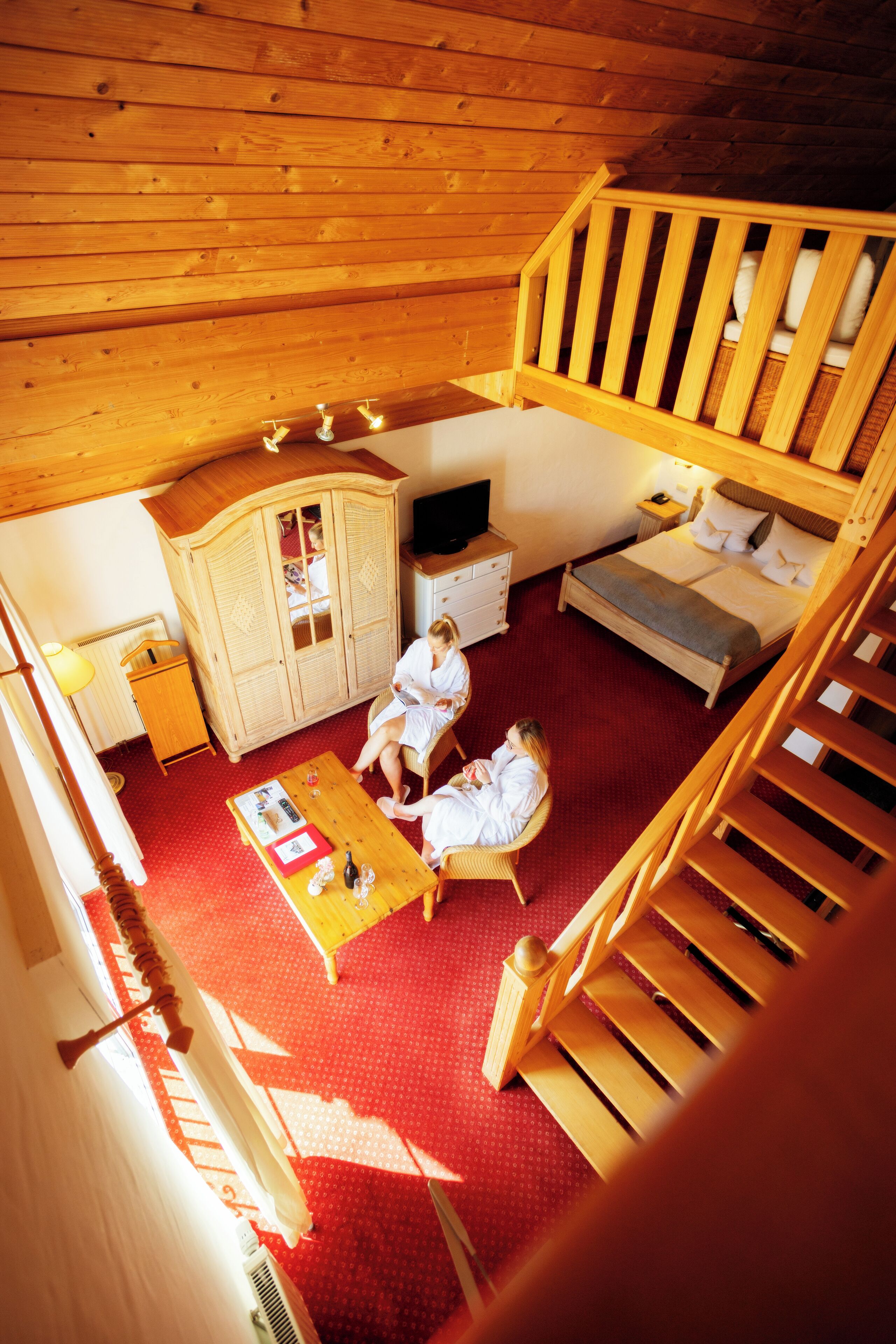 A wooden cabin with a loft bedroom, a dining area, and a wooden staircase.