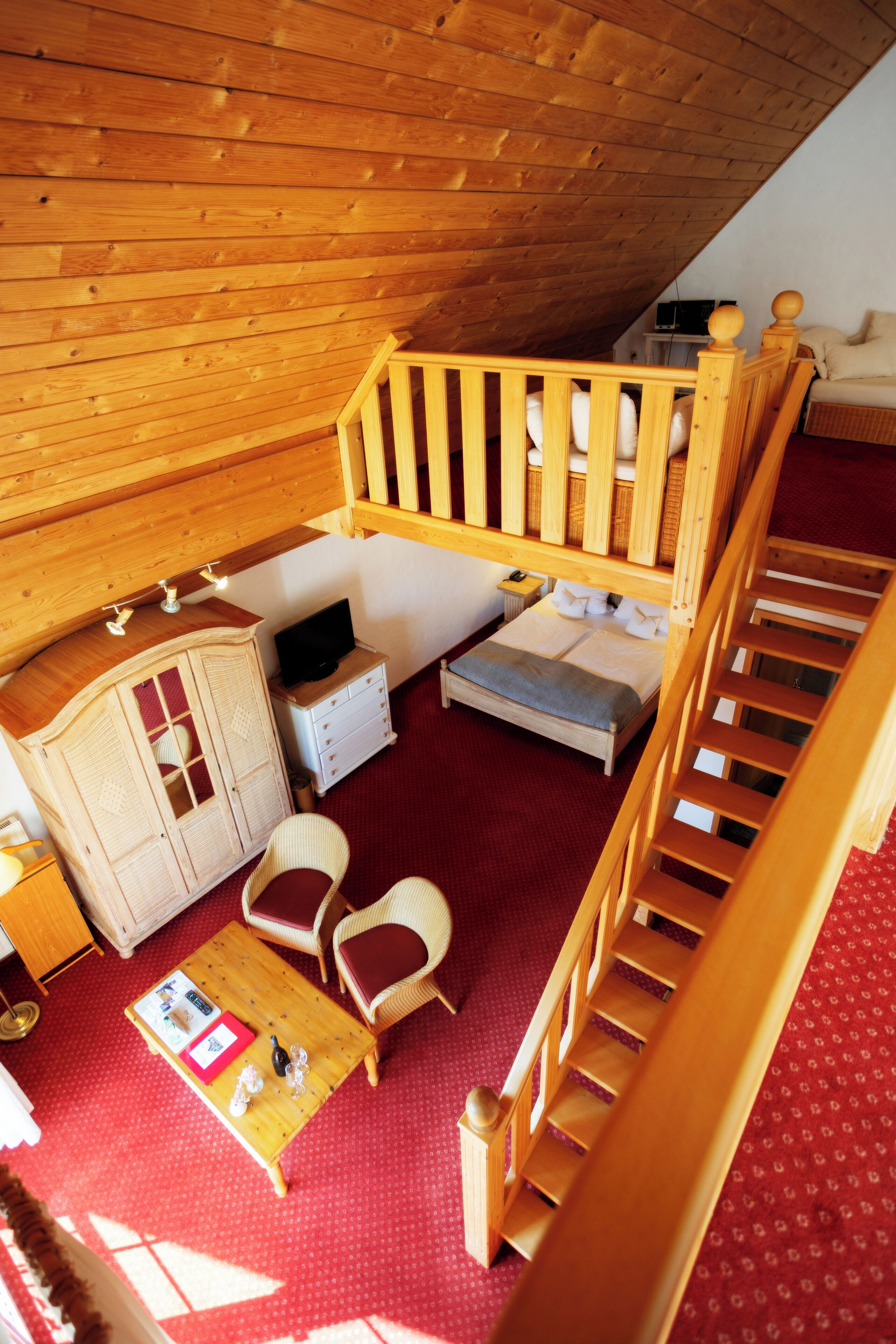 A loft bedroom with a wooden staircase, a bed, a desk, and a small seating area.