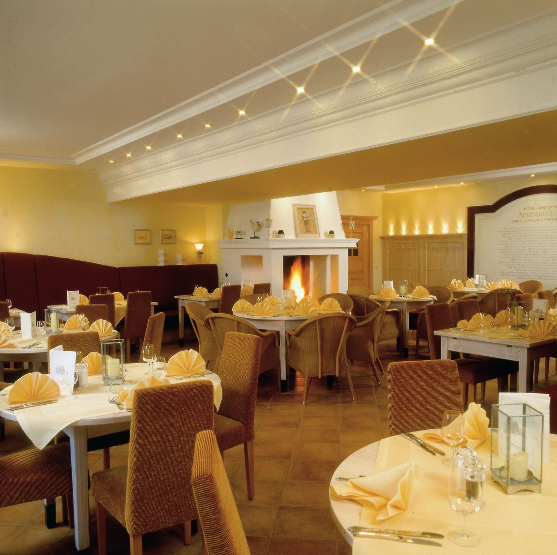 Een restaurant met ronde tafels, rieten stoelen en een open haard.