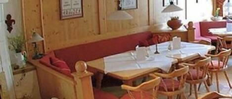 Un comedor acogedor con paredes de madera, un banco con cojines rojos y varias mesas con sillas.