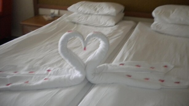 A hotel room with a neatly made bed featuring a swan-shaped towel arrangement. - The Southwold (Skegness)