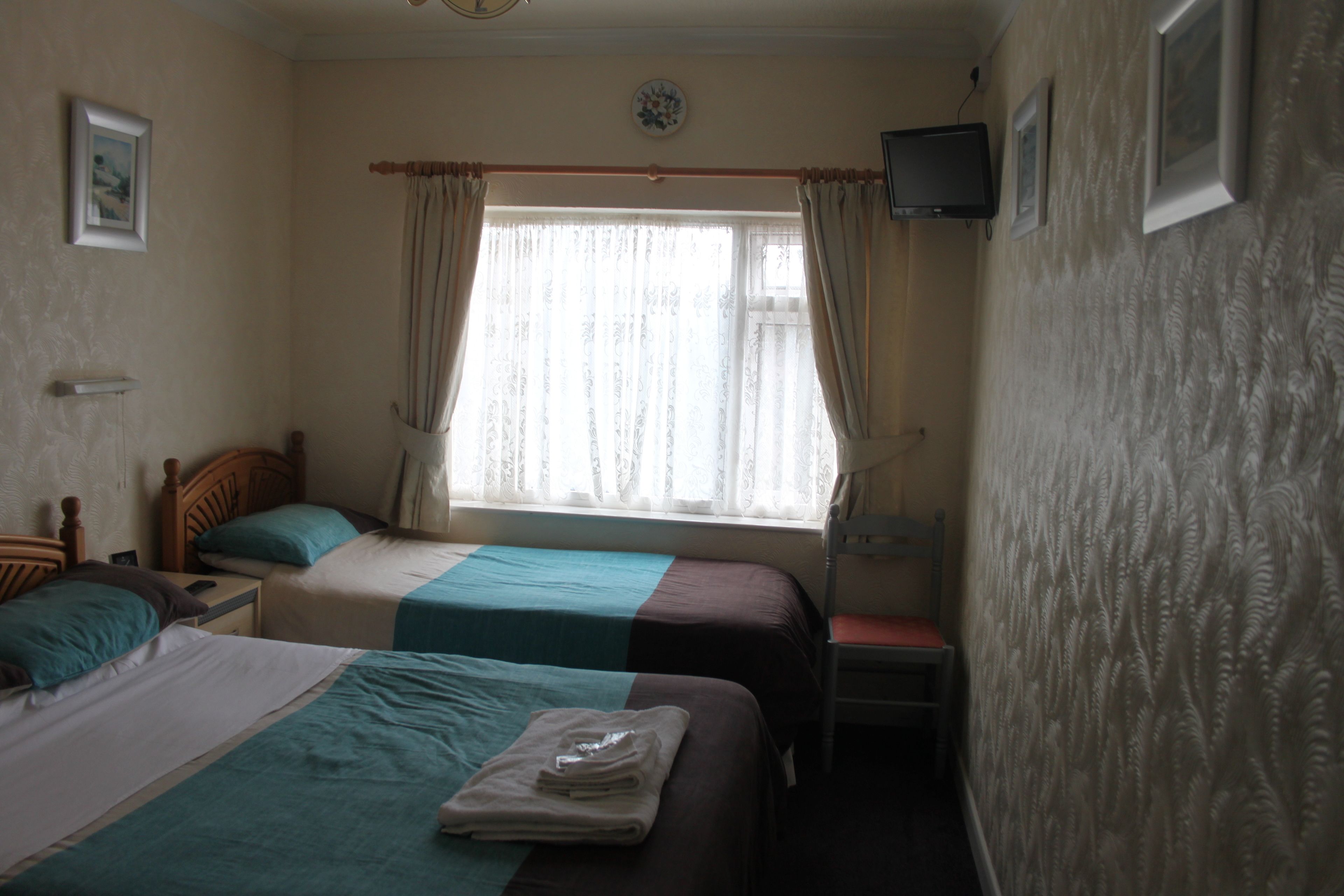 Een kamer met twee bedden, een raam met gordijnen, een flatscreen televisie en een klok aan de muur.