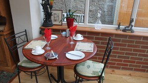 A round wooden dining table with four chairs, set with white plates, silverware, and red napkins. - The Southwold (Skegness)
