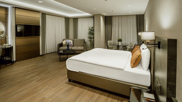 Una habitación de hotel moderna con una cama grande, un escritorio con lámpara, un televisor y una pequeña mesa con un florero.