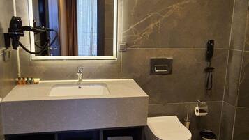 A modern bathroom with a large mirror, a sink, a toilet, and a trash can.