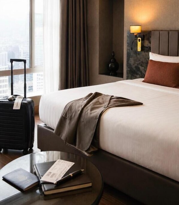 A hotel room with a bed, a suitcase, a nightstand, and a window with a view of buildings. - KIZILKAYA BUSINESS OTEL  (Korfez)