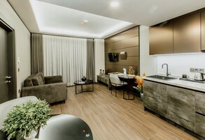 A modern kitchen with a built-in oven, a dining area with a table and chairs, and a living room with a sofa and a plant.