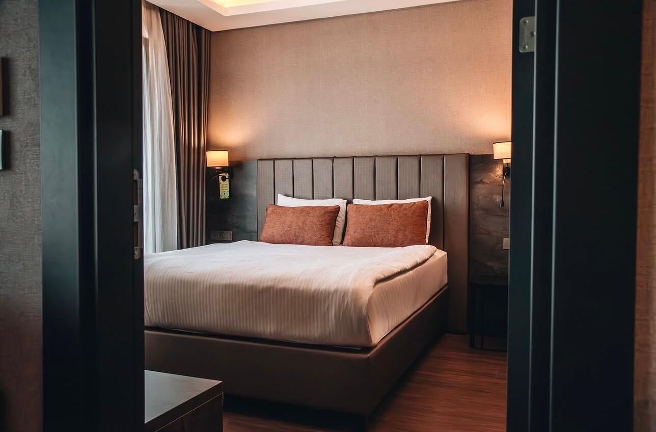 A hotel room with a large bed, two bedside lamps, a headboard, and a nightstand.
