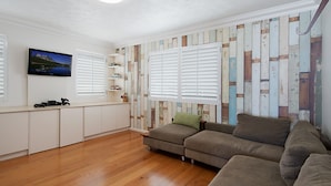 A modern living room with a wooden floor, a sectional sofa, a flat-screen TV, and a wall with a wooden plank design.