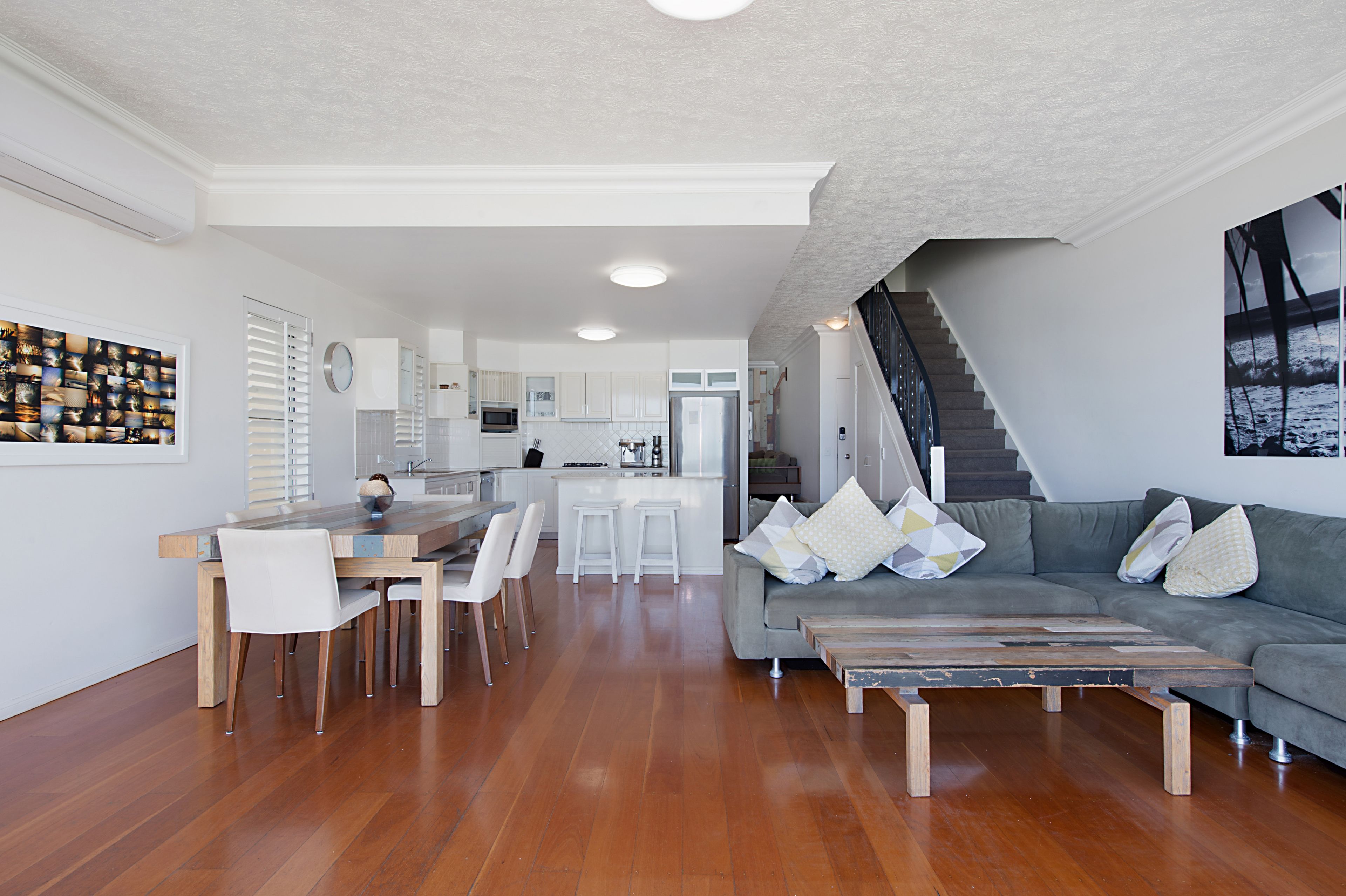 Ein modernes Wohnzimmer mit grauem Sofa, Couchtisch aus Holz und einem Essbereich mit Holztisch und weißen Stühlen.