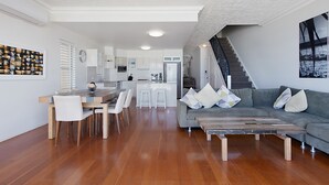 A modern living room with a grey sofa, wooden coffee table, and a dining area with a wooden table and white chairs.