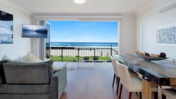 A modern living room with a large window overlooking the ocean, a dining table, and a gray sofa.