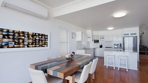 A modern kitchen with white cabinets, a central island with stools, and a dining table with chairs.
