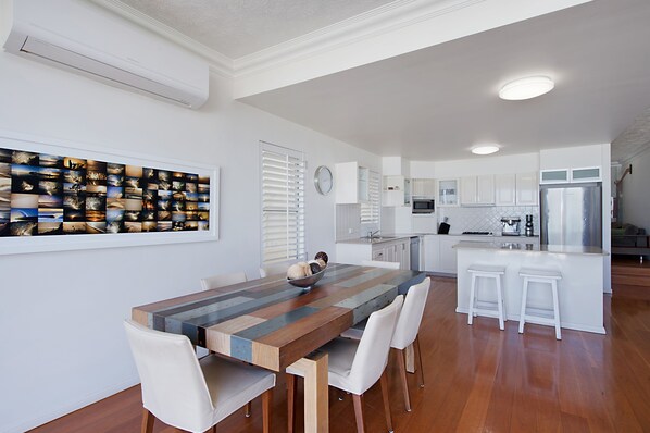 A modern kitchen with white cabinets, a central island with stools, and a dining table with chairs.