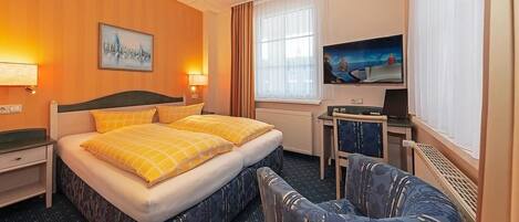 Een hotelkamer met een tweepersoonsbed, een bureau met een computer, een stoel, een televisie en een schilderij aan de muur.
