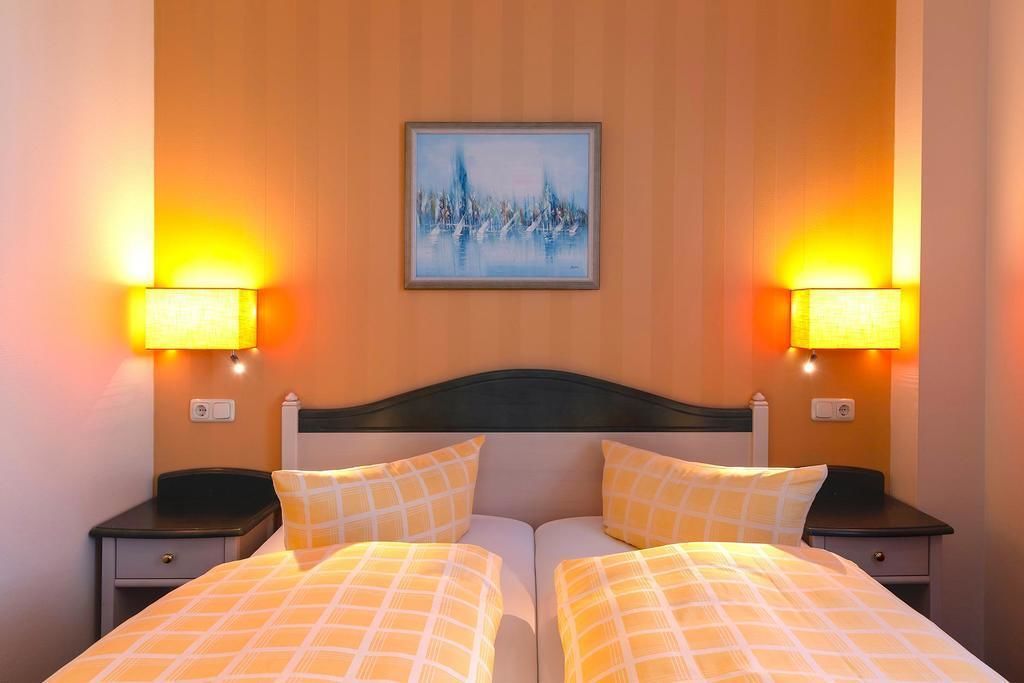 Una cama doble con cabecera, dos mesitas de noche y dos lámparas de pared.