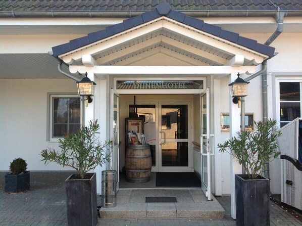 The entrance of Dunen Hotel with a traditional architectural style, featuring a welcoming entrance with a glass door and a small porch area. - Dünenhotel am Meer (Rostock)