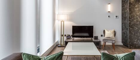 Een moderne woonkamer met een flatscreen televisie, een salontafel en een bank met groene kussens.