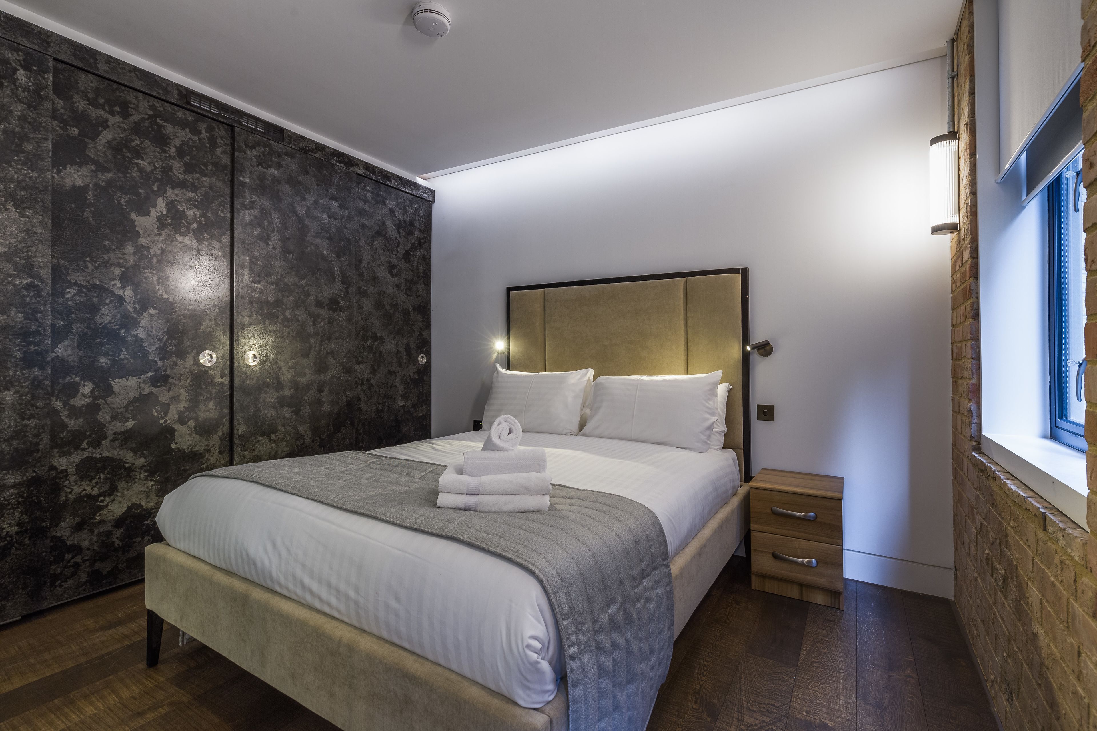 Een moderne slaapkamer met een groot bed, een houten nachtkastje, een kledingkast en een raam met uitzicht.