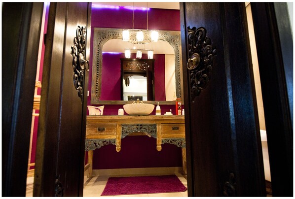 Casa de banho com toucador de madeira, espelho grande e tapete roxo.