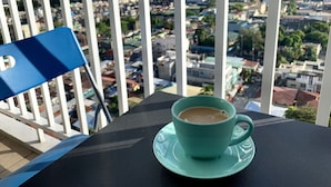 A balcony with a table and a chair, a cup of coffee, and a cityscape view. - Condo Unit With Balcony in Manila (Pasay)