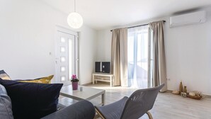 Un salon moderne avec un canapé, une table basse, un téléviseur posé sur un meuble et une grande fenêtre avec des rideaux.