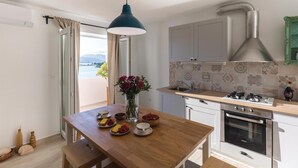 Une cuisine moderne avec vue sur la mer, une table à manger dressée et un grand luminaire suspendu.
